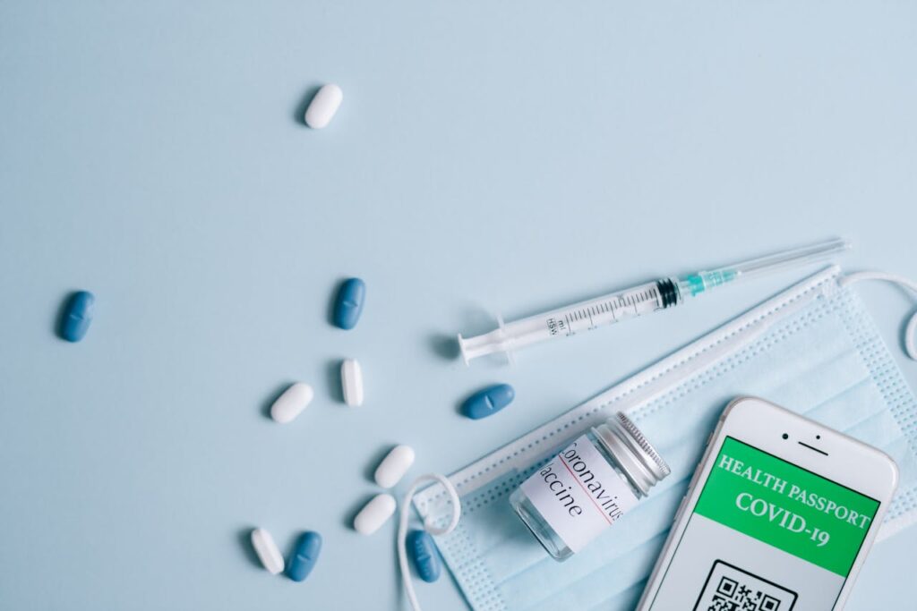 A flat lay of COVID-19 vaccination items including a mask, syringe, and health passport.